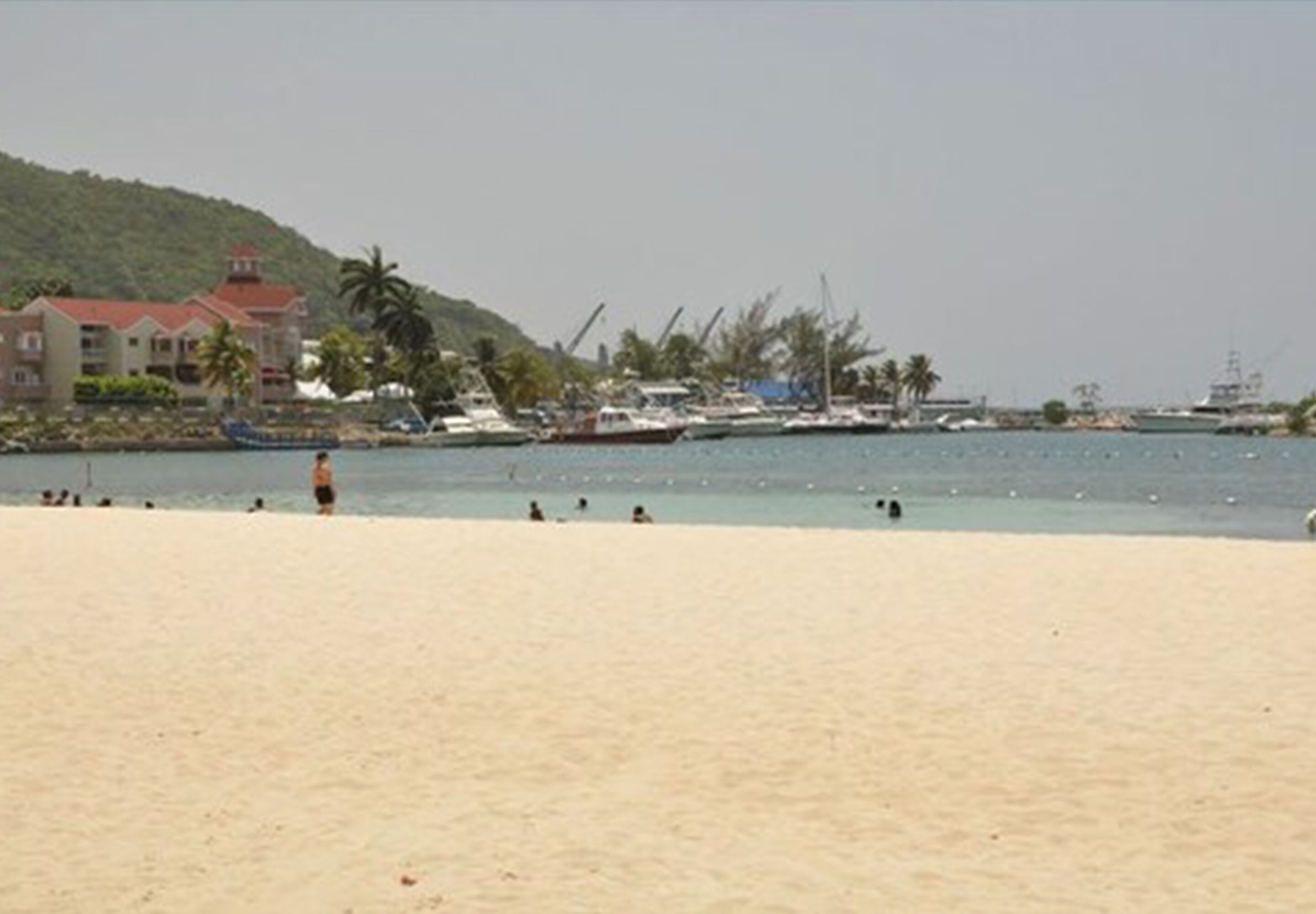 A beach with a sandy shore, a few people, and a building with a red roof in the background.