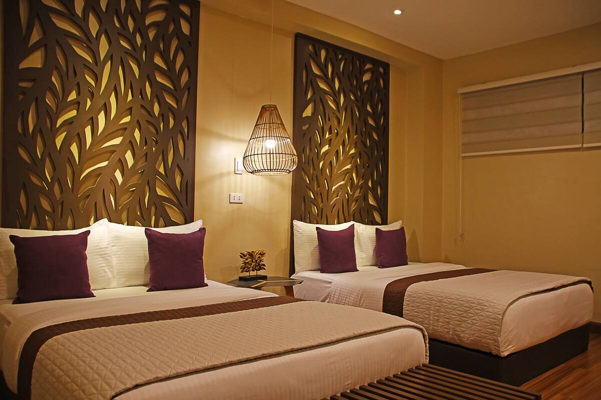 Una habitación de hotel con dos camas, cada una con cabecera, mesita de noche y un panel decorativo en la pared.