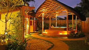 A wooden outdoor hot tub area with a thatched roof, surrounded by potted plants and a pathway. - Balai Princesa (Puerto Princesa)