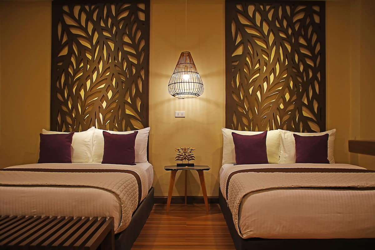 Habitación de hotel con dos camas, una mesita y un panel decorativo en la pared.