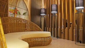 A room with a curved wicker sofa, tall floor lamps, and a wooden partition wall. - Balai Princesa (Puerto Princesa)