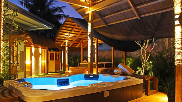 A hot tub under a wooden roof with a thatched ceiling, surrounded by wooden furniture and tropical plants. - Balai Princesa (Puerto Princesa)