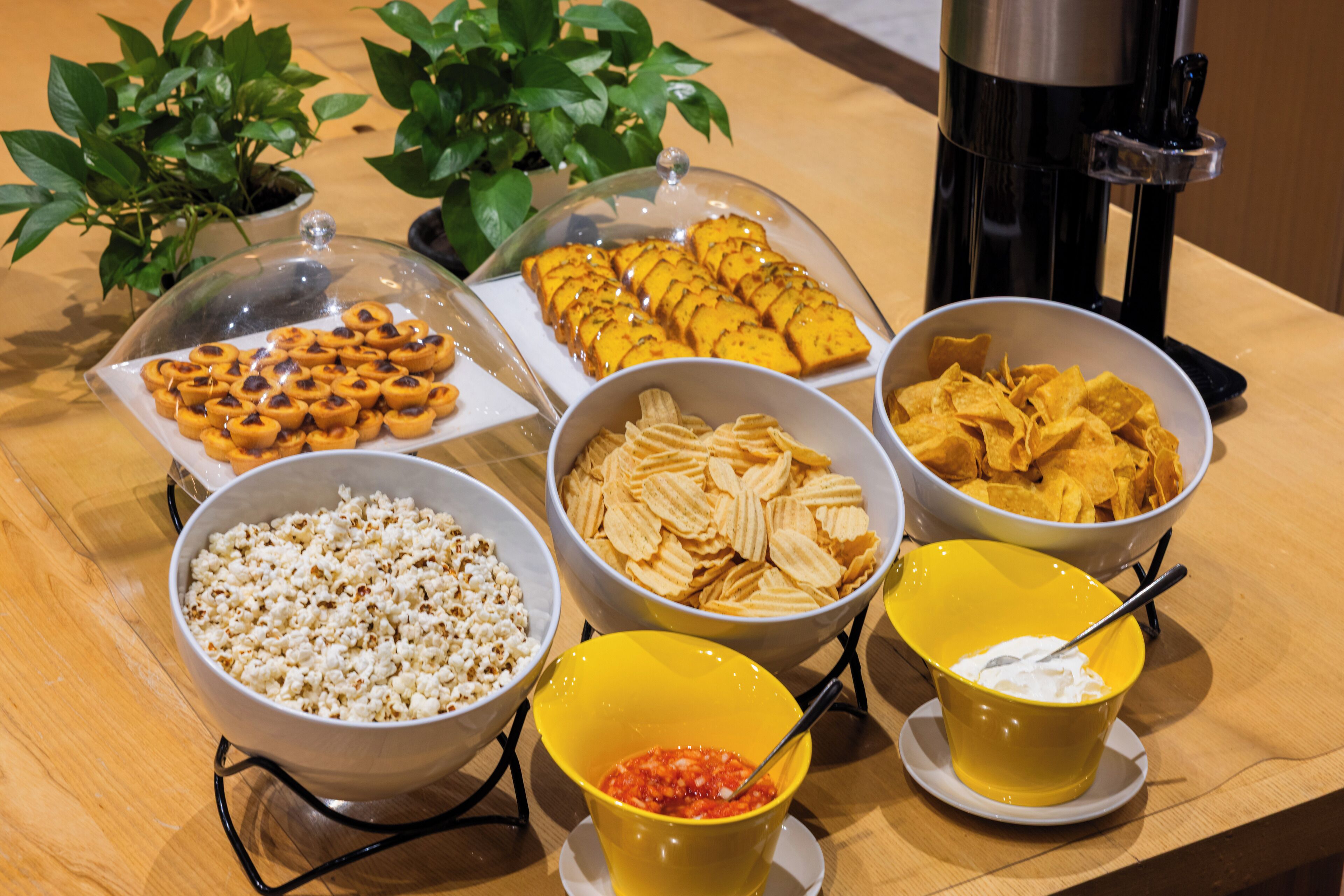 Uma mesa de buffet com diversos alimentos, incluindo pipoca, nachos e um recipiente com molho salsa.