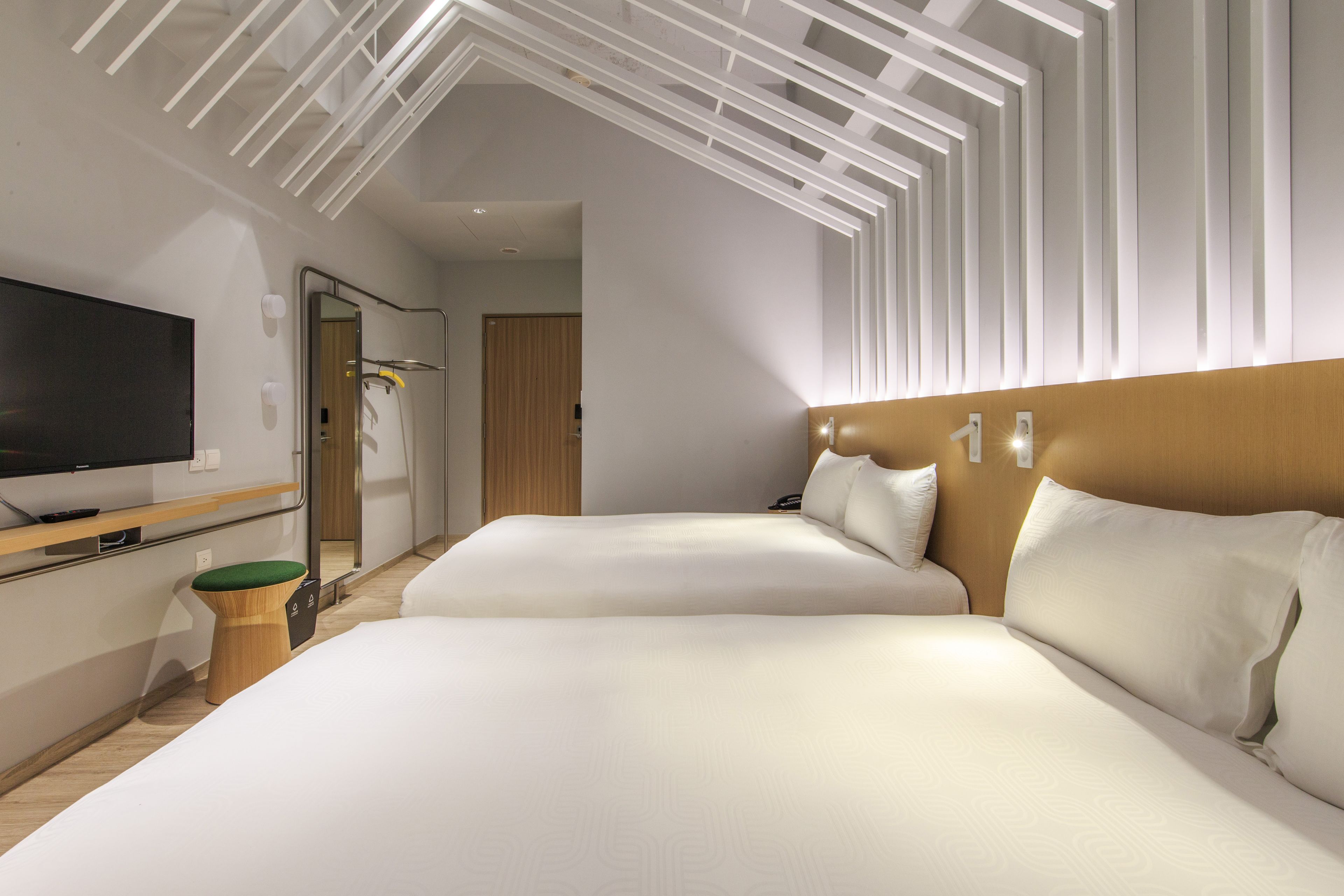 Une chambre d’hôtel moderne équipée de deux lits, d’un téléviseur à écran plat, d’une table de chevet en bois et d’un miroir.