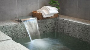 A bathtub with a waterfall feature, a wicker basket with folded towels, and a potted plant. - Hotel PIN Jiaoxi (Jiaoxi)