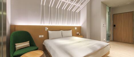 Una habitación de hotel moderna con una cama grande, un sillón verde, una pequeña mesa de madera y una lámpara de techo original.