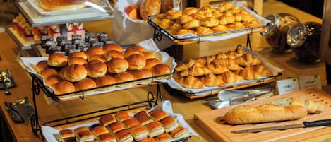 A buffet with various baked goods including rolls, pastries, and bread.