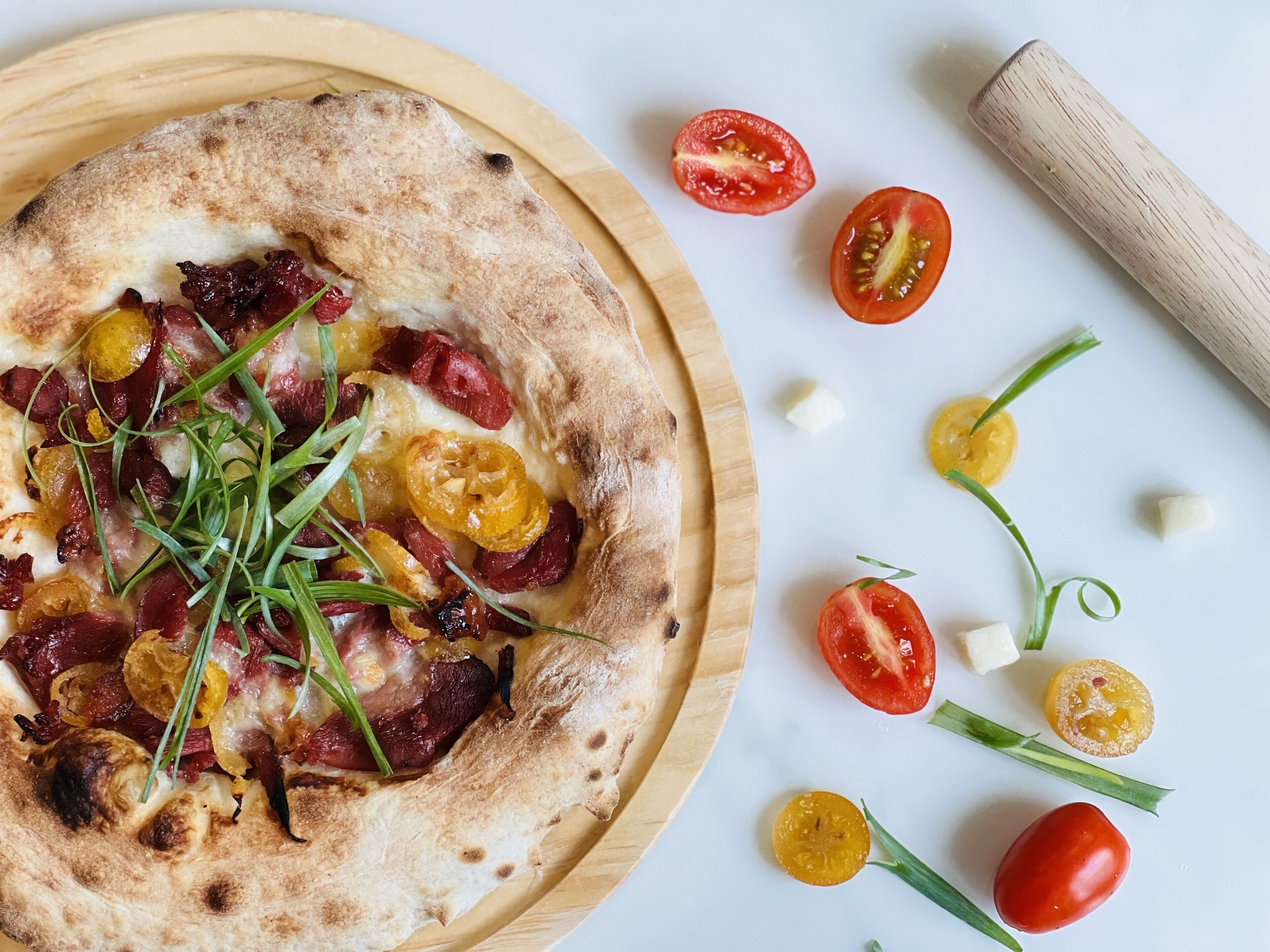 A pizza with various toppings on a wooden board, surrounded by cherry tomatoes and other vegetables.
