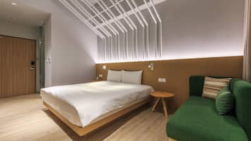 Una habitación de hotel moderna con una cama grande, un sofá verde y suelo de madera.