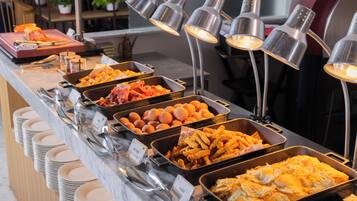 Ein Buffet mit verschiedenen Speisen und Besteck, darüber hängen Metalllampen.