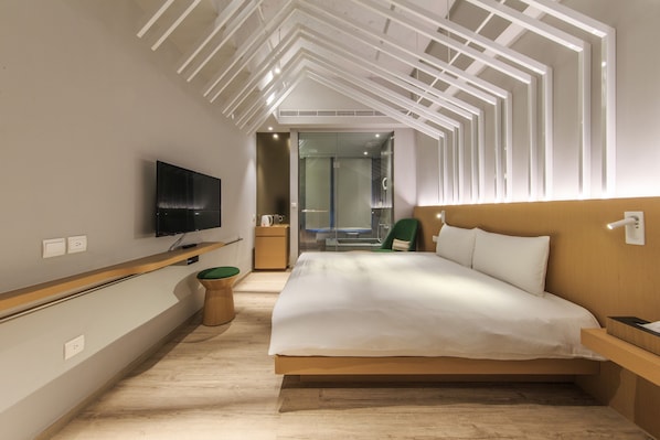 Una habitación de hotel moderna con una cama grande, un televisor montado en la pared y una mesita de noche de madera.