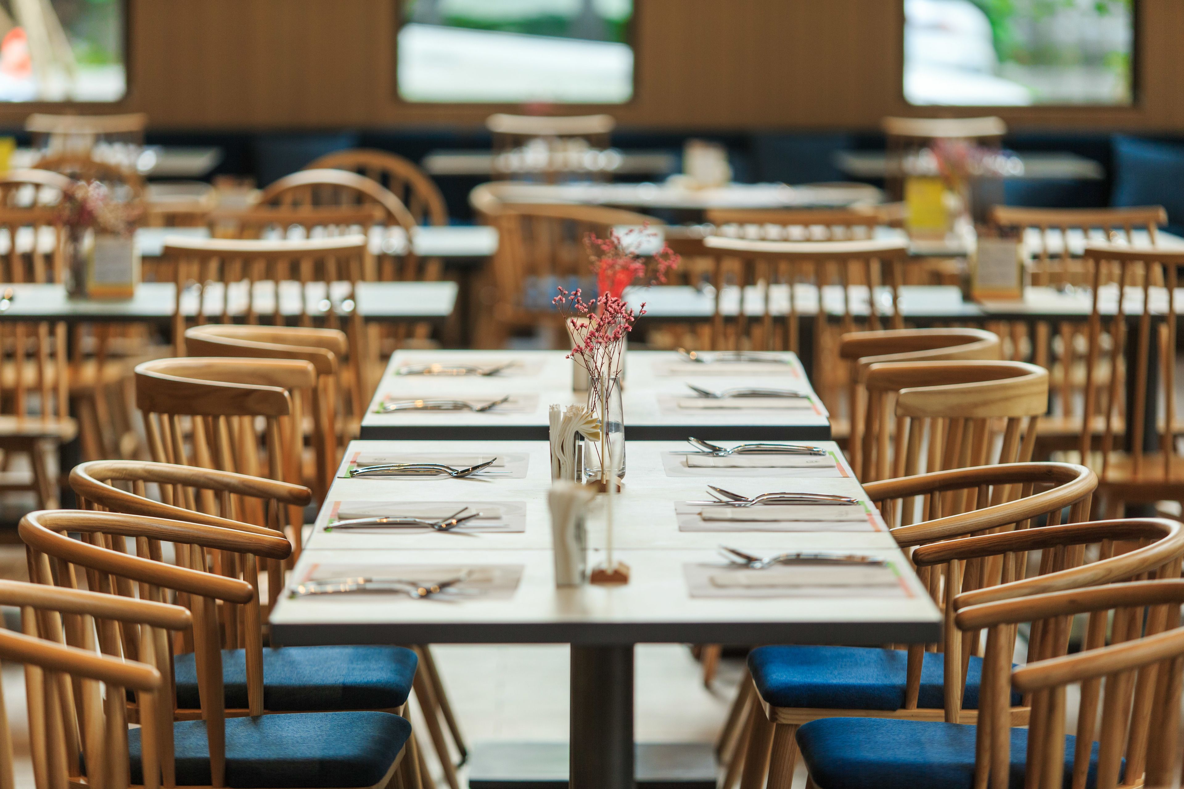 A restaurant with wooden chairs and tables, each set with cutlery and a vase of flowers.