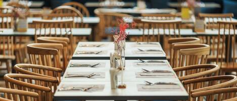 A restaurant with wooden chairs and tables, each set with cutlery and a vase of flowers.