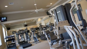 Une salle de sport équipée de divers appareils d’exercice, d’un tapis de course et d’un ventilateur de plafond.