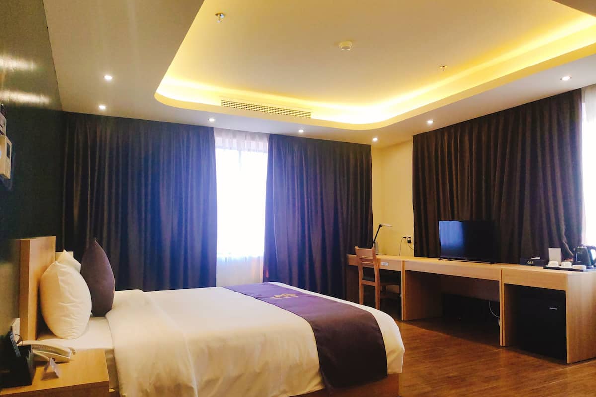 Ein Hotelzimmer mit Bett, Schreibtisch, Fernseher und einem Fenster mit Vorhängen.
