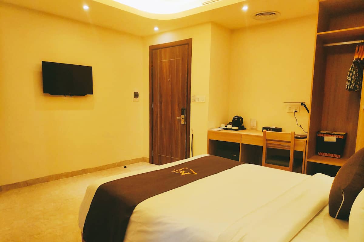 Ein Hotelzimmer mit Bett, Schreibtisch, Stuhl, Kleiderschrank und einem am Wand befestigten Flachbildfernseher.