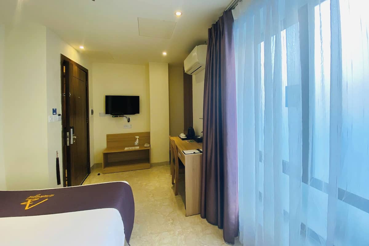 Ein Hotelzimmer mit Bett, Schreibtisch, Fernseher und einem Fenster mit Vorhängen.