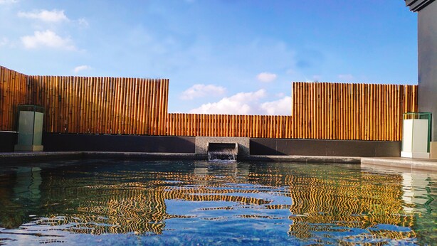 A pool with a bamboo wall and a clear sky.