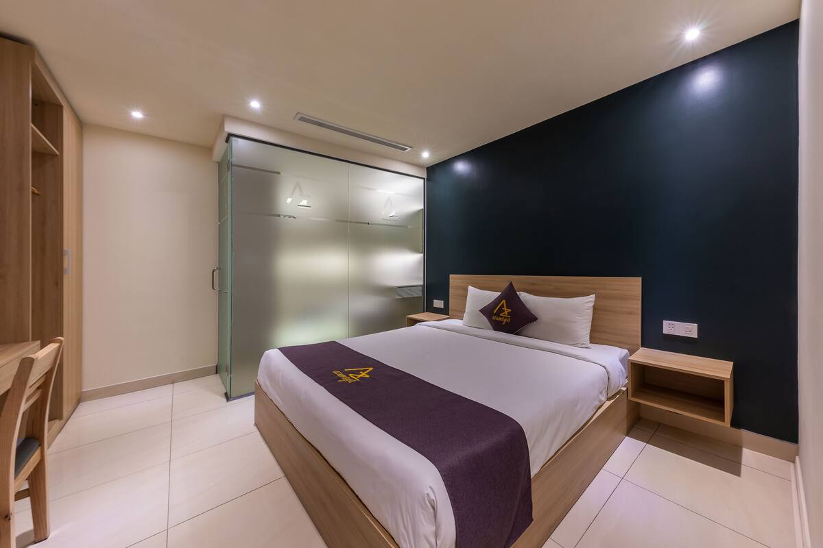 Ein modernes Hotelzimmer mit einem großen Bett, einem Holztisch, einem Kleiderschrank und einem Schrank mit Glastüren.