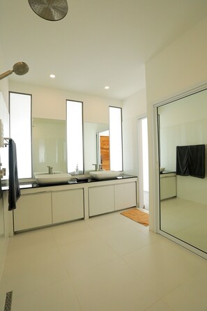 Un baño moderno con un espejo grande, dos lavamanos y zona de ducha.