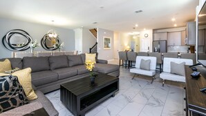 A modern living room with a gray sofa, a coffee table, and a dining area with white chairs. - Storey Lake Exec Villas- 2965fs (Kissimmee)