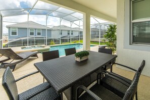 Een overdekt buitengebied met een zwembad, lounge stoelen en een tafel met stoelen.