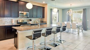 A modern kitchen with dark cabinets, a granite countertop, and a central island with bar stools. - Champions Gate Home 2 U- Thor - Cg1561 (Davenport)