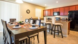 Une cuisine moderne avec des meubles en bois, un îlot central et un coin repas comprenant une longue table et des chaises.