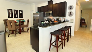 A modern kitchen with dark wood cabinets, a stainless steel refrigerator, and a central island with bar stools. - Veranda Palms Home 2 U- Spider Man (Kissimmee)