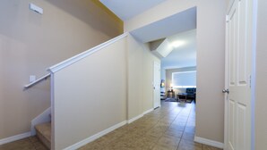 A hallway with a staircase leading to a landing, a kitchen area in the background, and a door on the right.