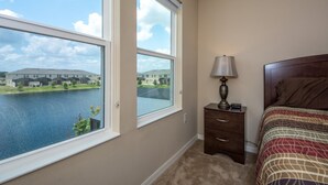 A bedroom with a large window, a bedside lamp, a wooden headboard, and a view of a building across a body of water.