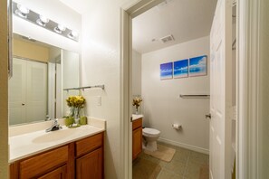 Ein Badezimmer mit Waschtisch, Spüle, Spiegel und Toilette. Zwei Wandleuchten befinden sich über dem Spiegel, und eine Handtuchstange ist an der Wand angebracht.