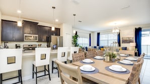 A modern kitchen with dark cabinets, a microwave, and a dining area with a large table set for six. - Storey Lake Exec Villas- 4811ll (Kissimmee)