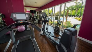 A gym with cardio machines, weight equipment, and a large window overlooking a pool area. - Lucaya Village Home 2 U- Anna (Kissimmee)