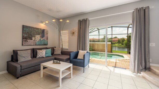Ein modernes Wohnzimmer mit einem Ecksofa, einem Couchtisch und Blick auf ein Schwimmbecken durch große Glasüren.