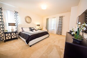 A bedroom with a bed, bedside tables, a mirror, curtains, and a desk with a plant. - Solterra Home 2 U- Apollo (Davenport)
