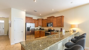 A kitchen with granite countertops, wooden cabinets, a built-in microwave, and a stainless steel refrigerator. - Champions Gate Home 2 U- Zeus (Davenport)