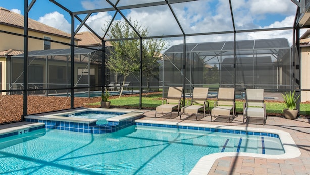 A swimming pool with a hot tub, surrounded by lounge chairs and a covered patio area. - Champions Gate Home 2 U- Zeus (Davenport)