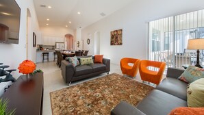 Een moderne woonkamer met een bank, twee oranje fauteuils, een salontafel en een keuken op de achtergrond.
