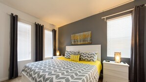 Een slaapkamer met een groot bed, een nachtkastje, een lamp en een schilderij aan de muur.