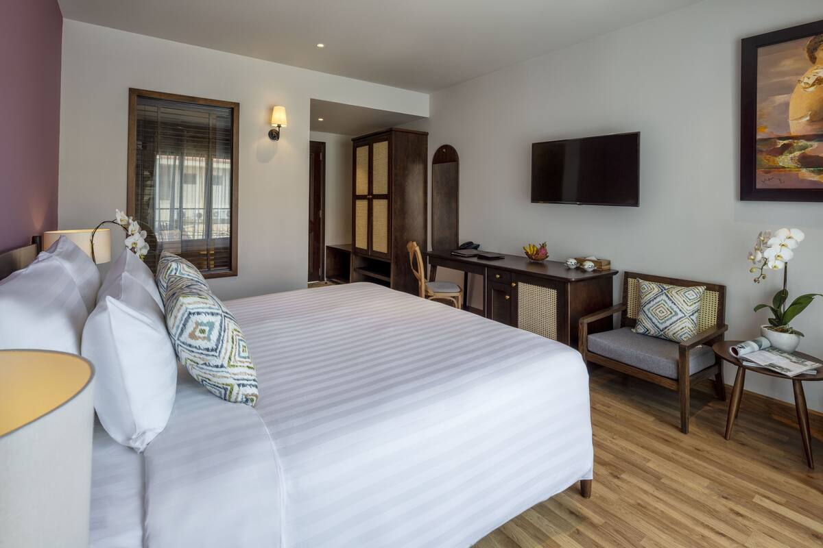 Een hotelkamer met een groot bed, een bureau, een stoel, een televisie en een potplant.