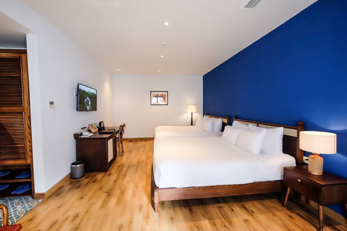 Een slaapkamer met een groot bed, houten vloer, een bureau met stoel, een televisie en een blauwe accentmuur.