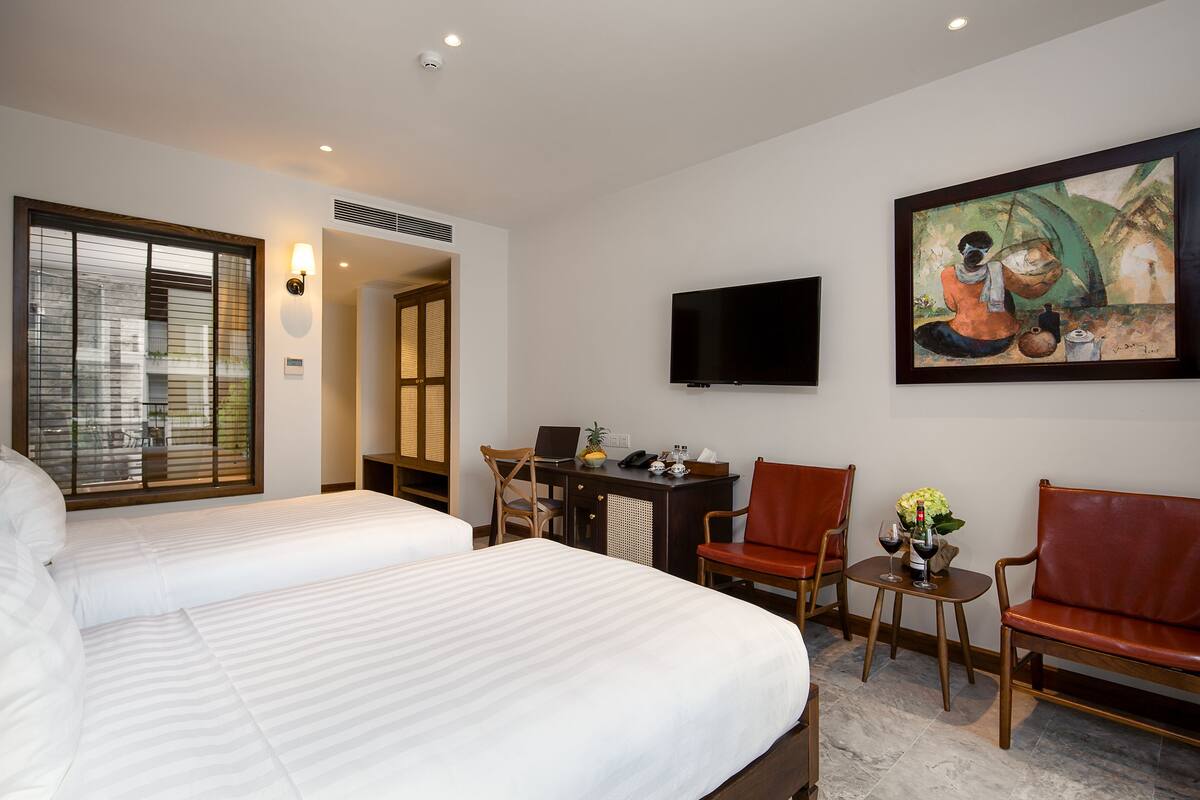 Hotelkamer met twee bedden, een bureau met een laptop, een televisie en een schilderij aan de muur.
