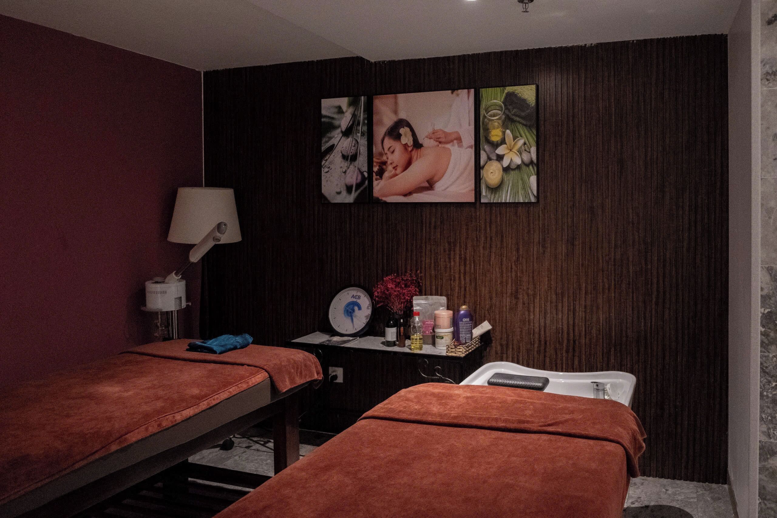A spa room with two massage tables, a clock, and a wall-mounted shelf with various items.