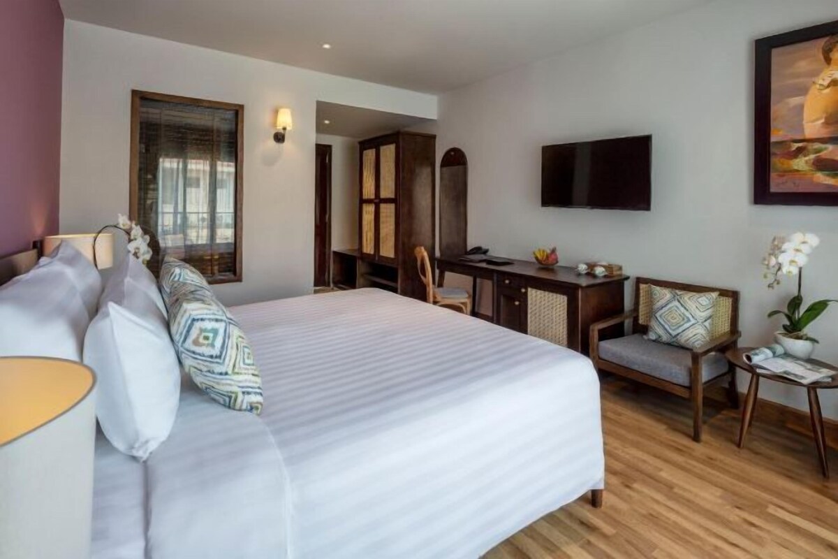 A hotel room with a large bed, a desk, a chair, a TV, and a small table with a plant.