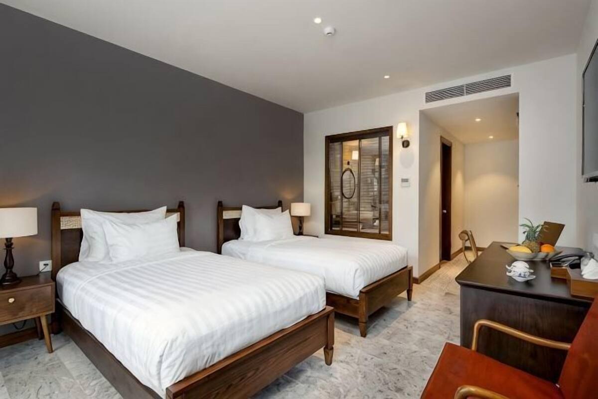 Een hotelkamer met twee bedden, een bureau, een stoel en een deur naar een andere kamer.