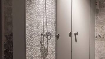 A walk-in shower with patterned tiles, a marble floor, and a trash bin to the right.