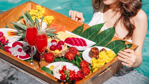 A person sitting by a pool with a tray of food and drinks.