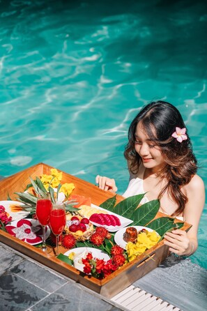 Une personne assise au bord d’une piscine, avec un plateau rempli de nourriture et de boissons.