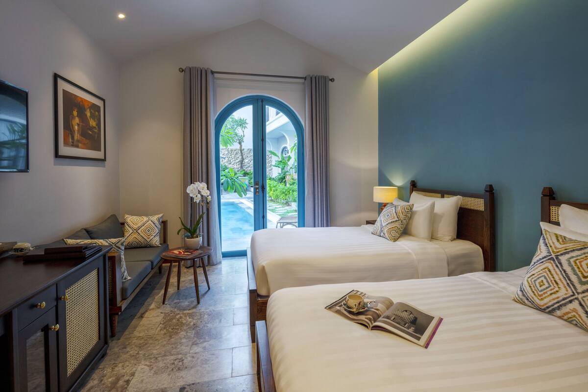 Een hotelkamer met twee bedden, een bureau, een kamerplant en uitzicht op de omgeving.